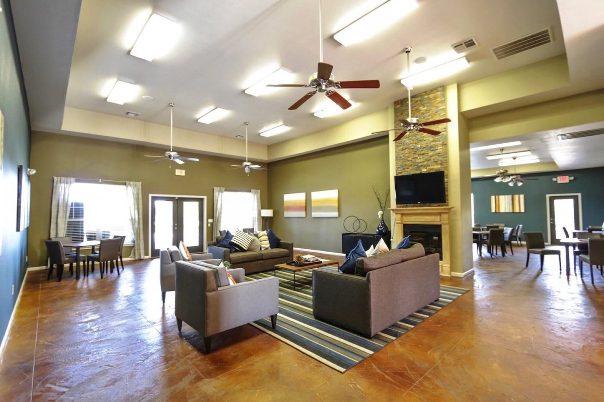 A spacious and modern living room featuring comfortable seating, a fireplace, and ceiling fans under bright lighting.
