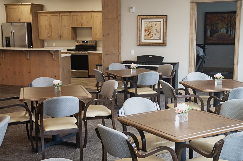 A modern dining area with wooden tables and cushioned chairs, adjacent to a kitchen.