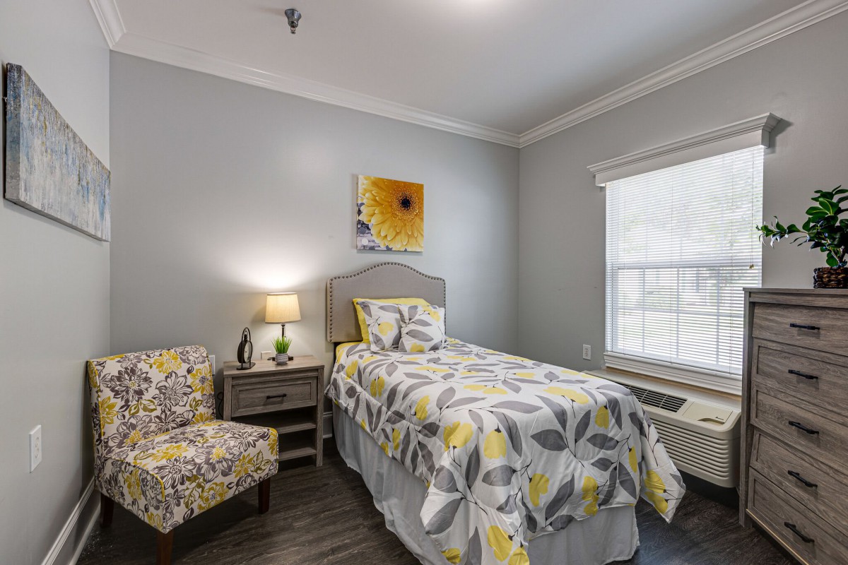 A cozy bedroom with a single bed featuring floral bedding, complemented by a matching chair and a nightstand with a lamp.
