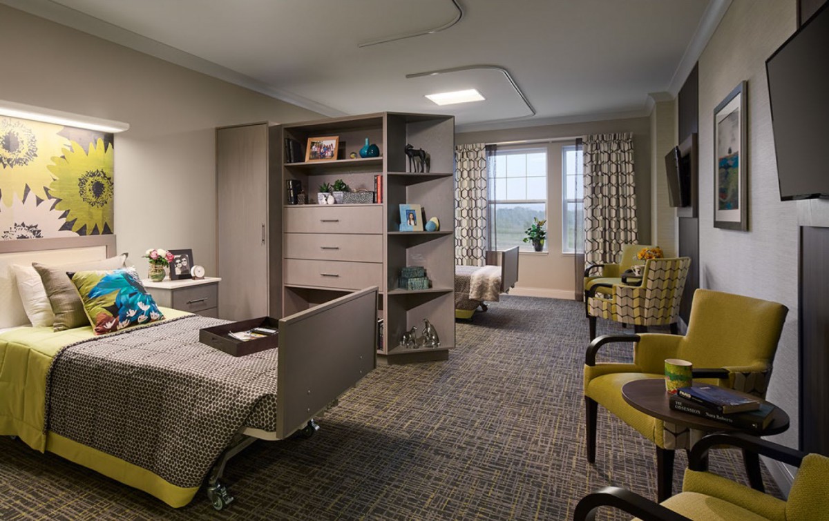 A cozy and well-organized bedroom featuring a bed, shelves, seating area, and large windows with curtains.