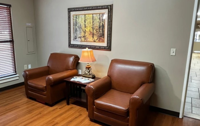 A cozy corner featuring two brown leather armchairs, a lamp, and a nature painting.