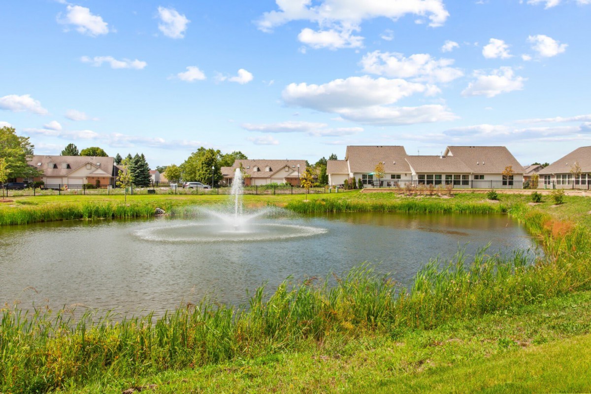 A peaceful residential area with a pond and fountain under a clear, blue sky.