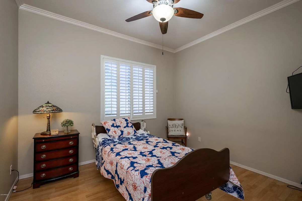 A cozy bedroom with a single bed and floral bedding, complemented by wooden flooring and a ceiling fan.