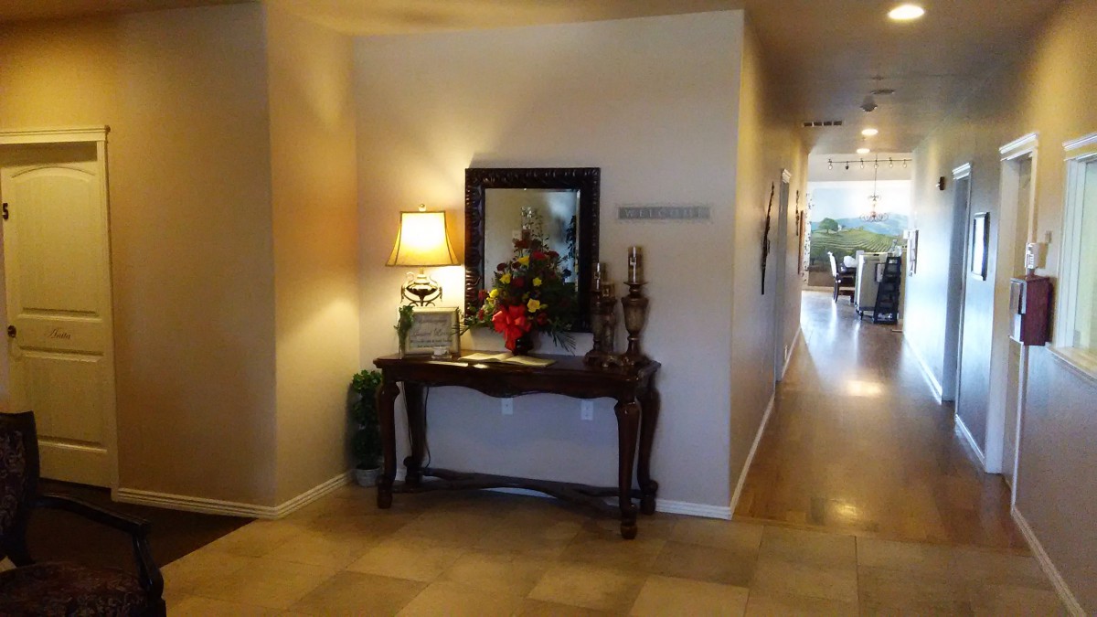 A warmly lit entryway with a decorative table, featuring a lamp, mirror, floral arrangement, and candles.