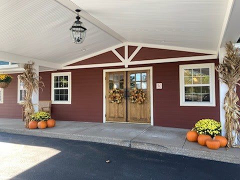 An entrance decorated with pumpkins and fall wreaths, featuring a wooden door on a red building.
