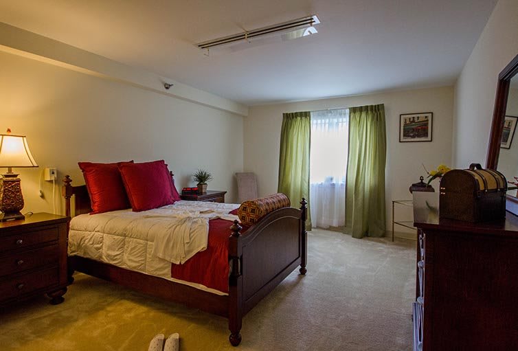 A cozy bedroom with a wooden bed, red pillows, and green curtains.