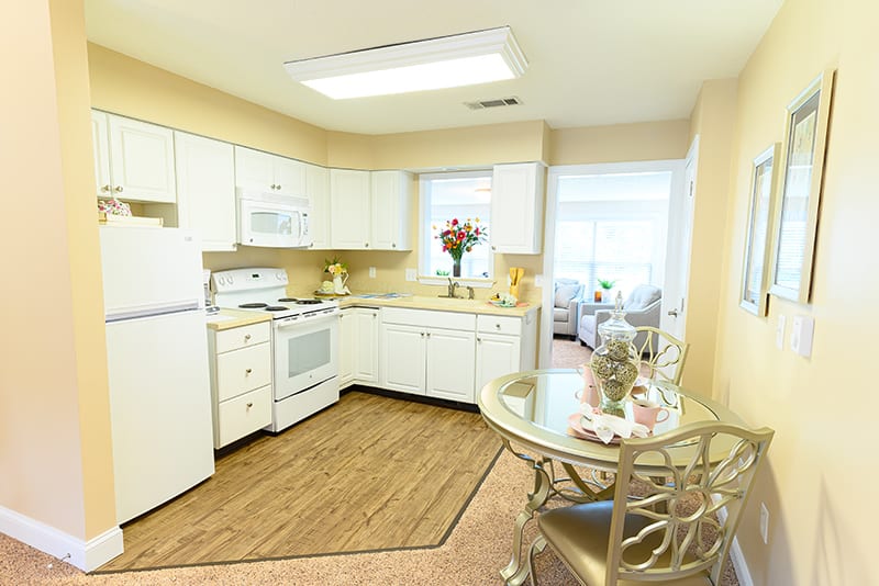 A modern kitchen with white cabinets, a dining area, and bright lighting.