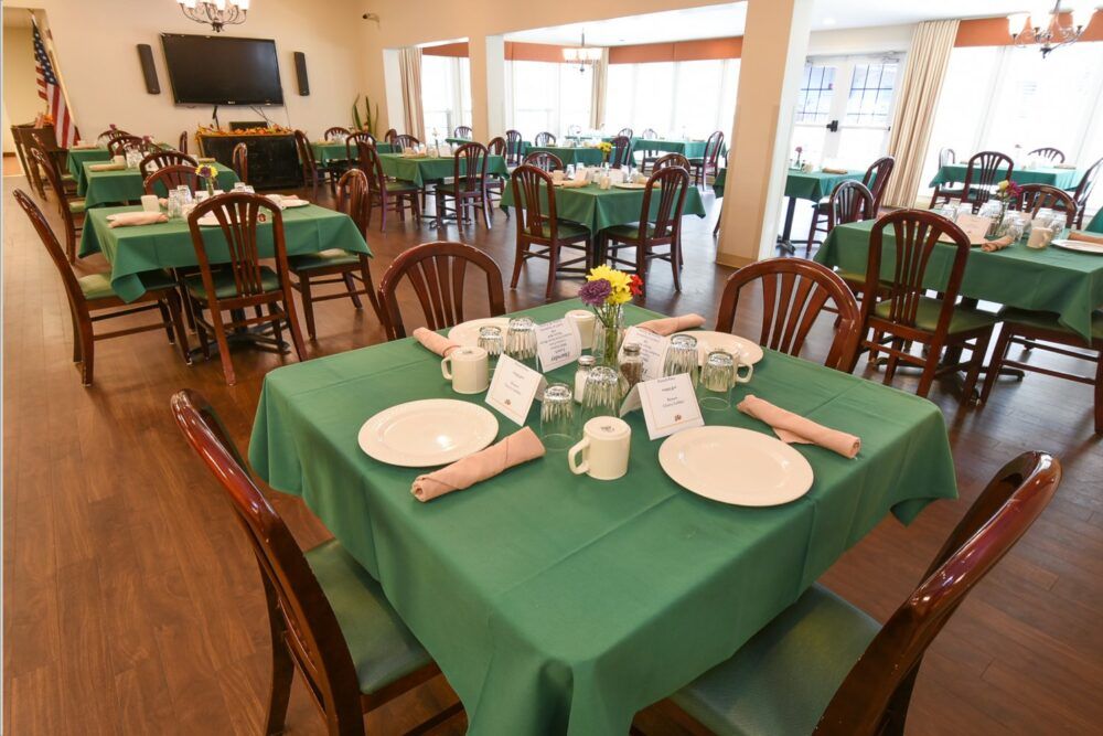 A well-arranged dining area with tables set for guests, featuring green tablecloths and wooden chairs.