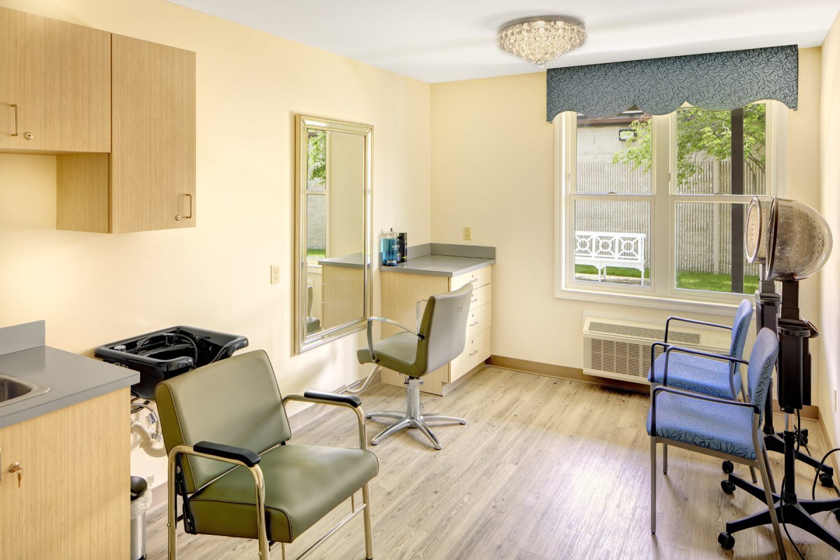 A well-lit hairdressing salon with stylish chairs, a large mirror, and a window providing natural light.