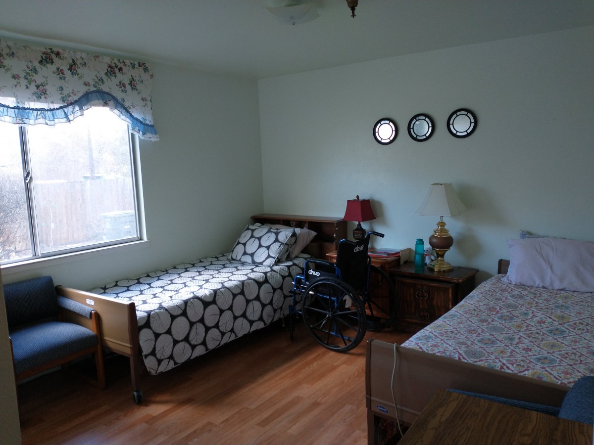 A cozy bedroom with two single beds and a wheelchair, featuring wall decorations and a lamp.