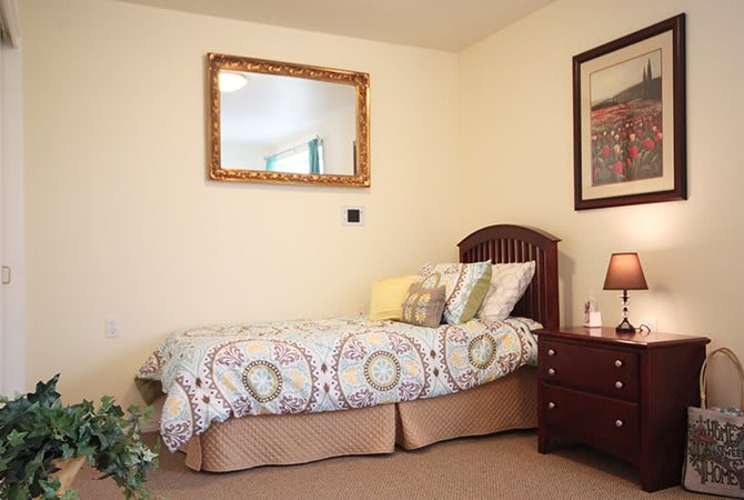 A neatly arranged bedroom with a single bed, nightstand, mirror, and decor.
