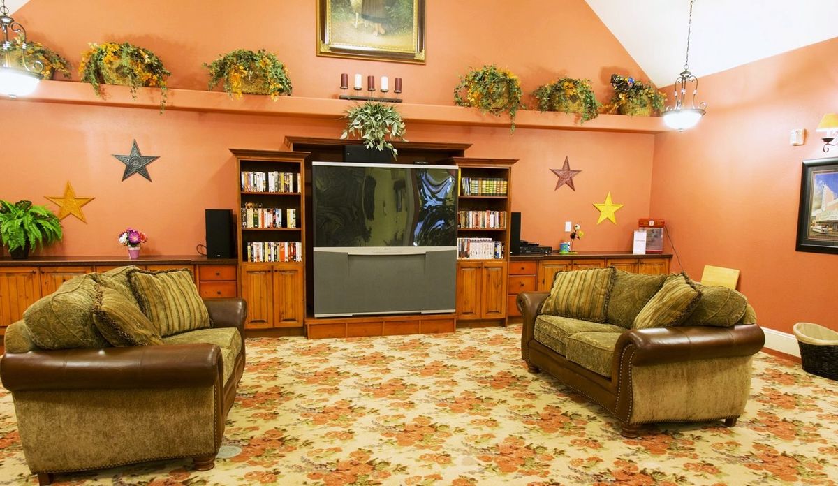 A vintage-style living room with a large television, wooden shelves, floral carpet, and comfortable sofas.