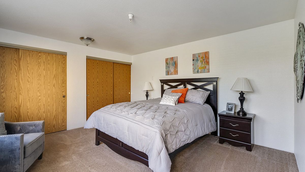 A cozy bedroom with a neatly made bed, nightstand, lamps, and a closet with sliding doors.