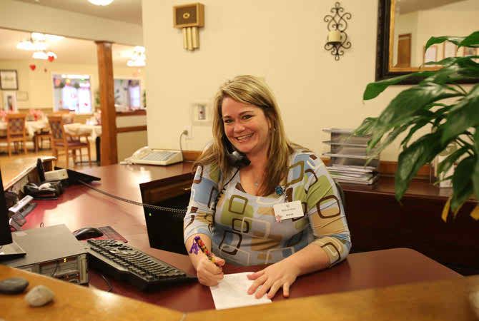 A receptionist smiling at her desk while using a telephone headset.