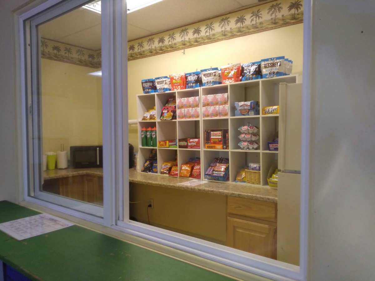 View through a window into a room with shelves stocked with various snacks and candy.