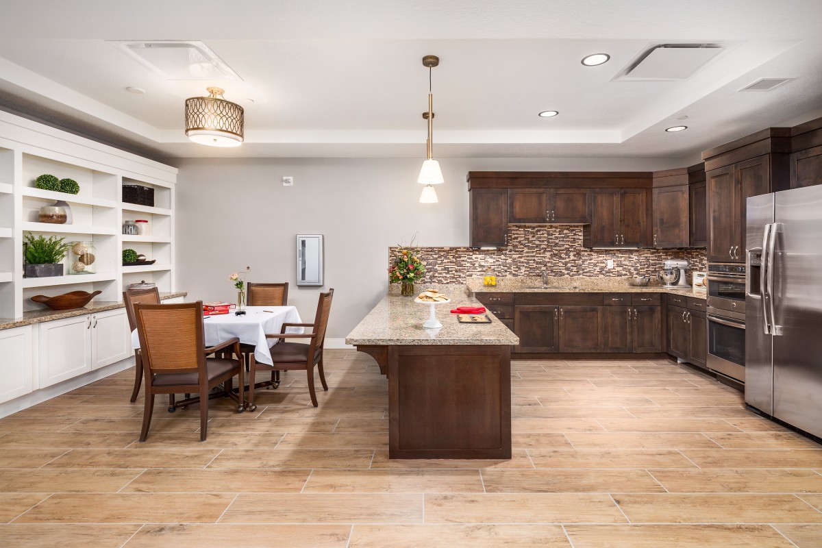 A modern kitchen with a wooden dining area, featuring a central island and elegant pendant lighting.