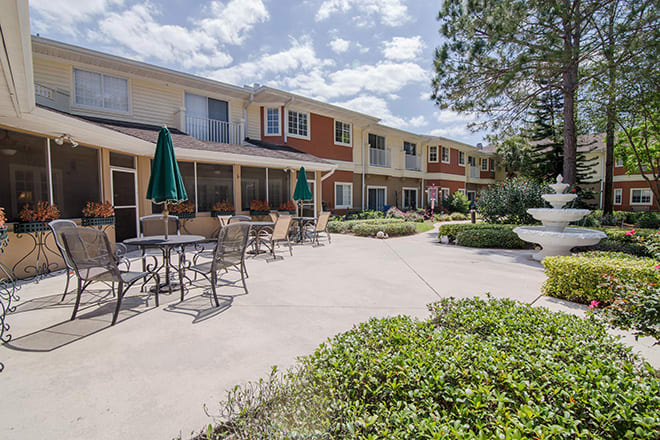 A sunny outdoor patio area with tables, chairs, and umbrellas in front of a residential building.