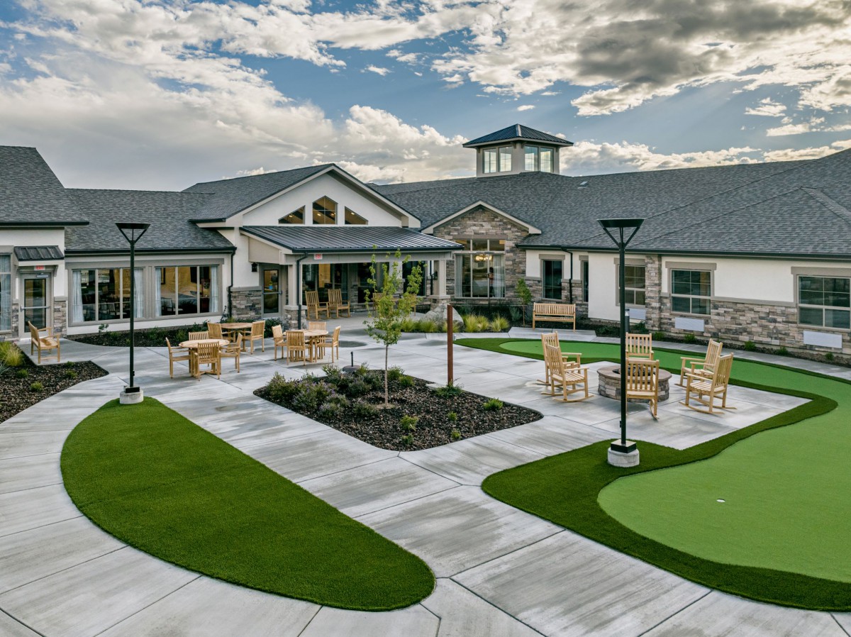 A modern building with a well-maintained courtyard featuring outdoor seating and green landscape.