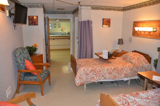 A cozy patient room in a healthcare facility, featuring two beds and comfortable seating.