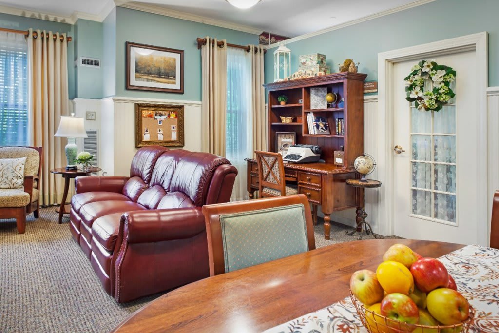A cozy living room with a leather sofa, wooden desk, and bookshelves.