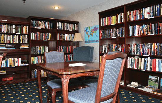 A cozy library room with bookshelves, a wooden table, and upholstered chairs.
