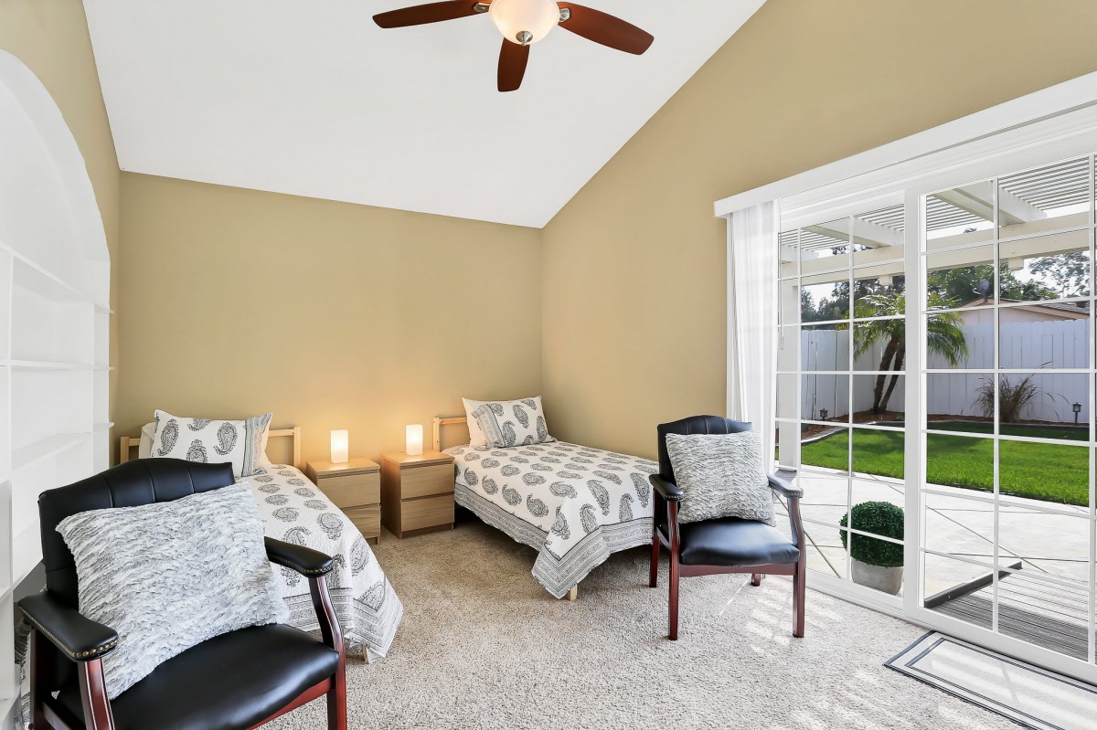 A well-lit bedroom featuring twin beds, neutral decor, and a sliding glass door opening to the outside.