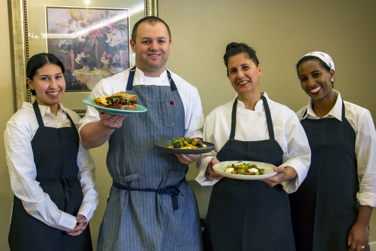 A group of chefs proudly presenting their dishes in a kitchen setting.