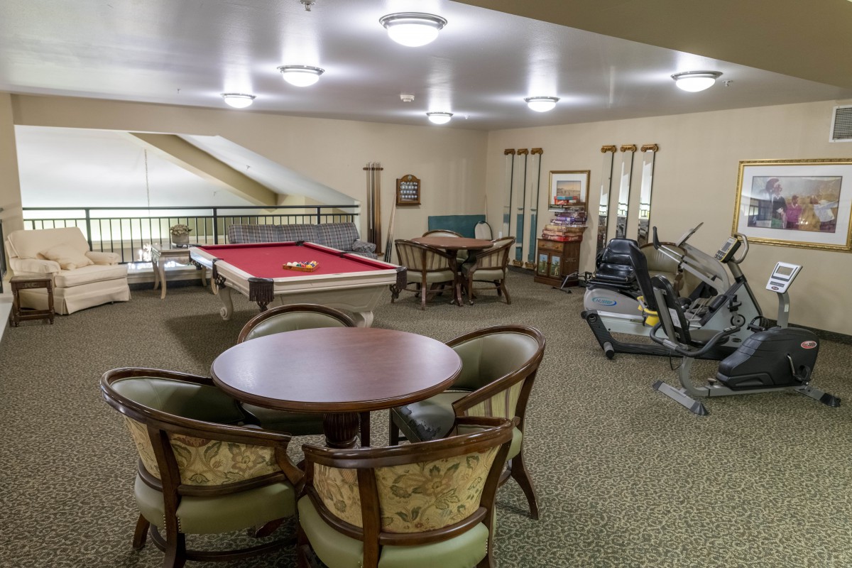 A recreation room featuring a pool table, exercise equipment, and a seating area.