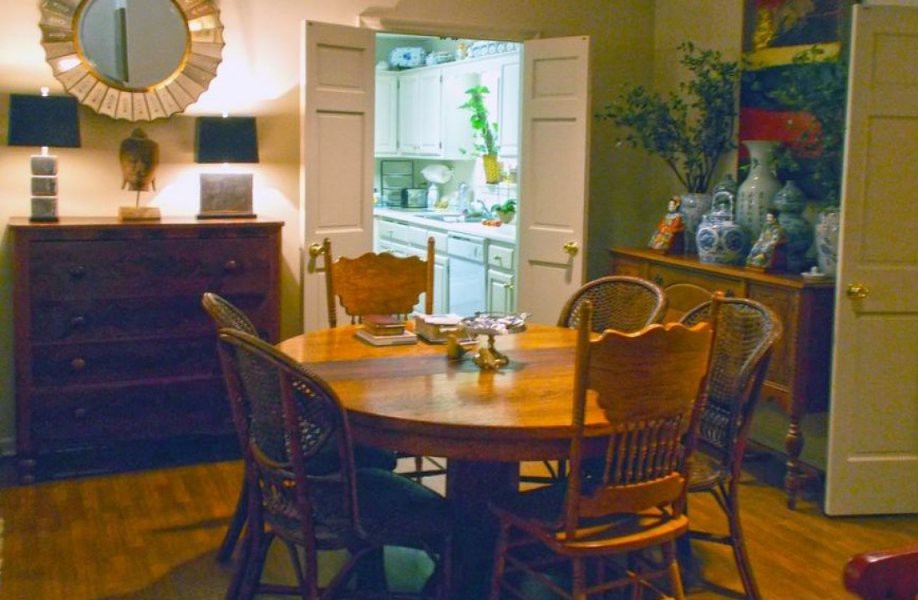 A cozy dining room with a wooden table and chairs, offering a peek into the kitchen through an open door.