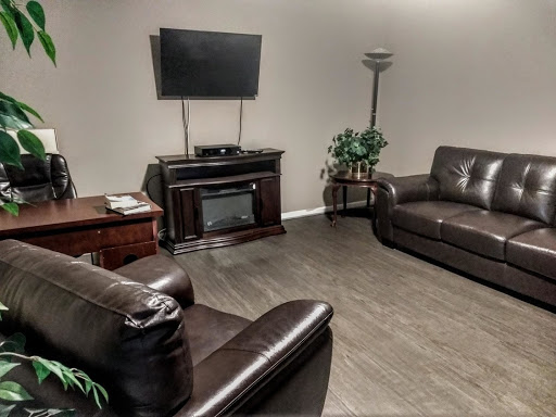 A cozy living room setup featuring dark leather sofas, a TV mounted on the wall, and a warm ambiance.