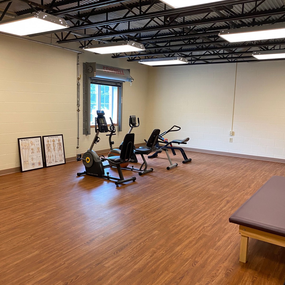 A gym room with exercise equipment and wooden flooring.