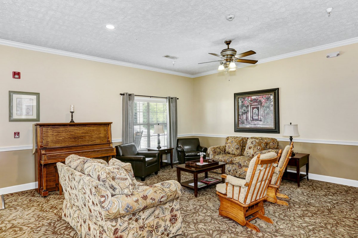 A cozy living room with floral-patterned furniture, a piano, and a ceiling fan.