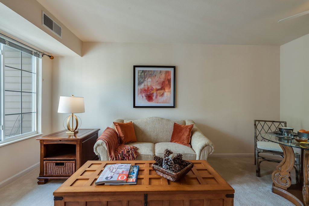 A cozy living room featuring a sofa with decorative pillows, a wooden coffee table with magazines and decor, and a lamp beside it.