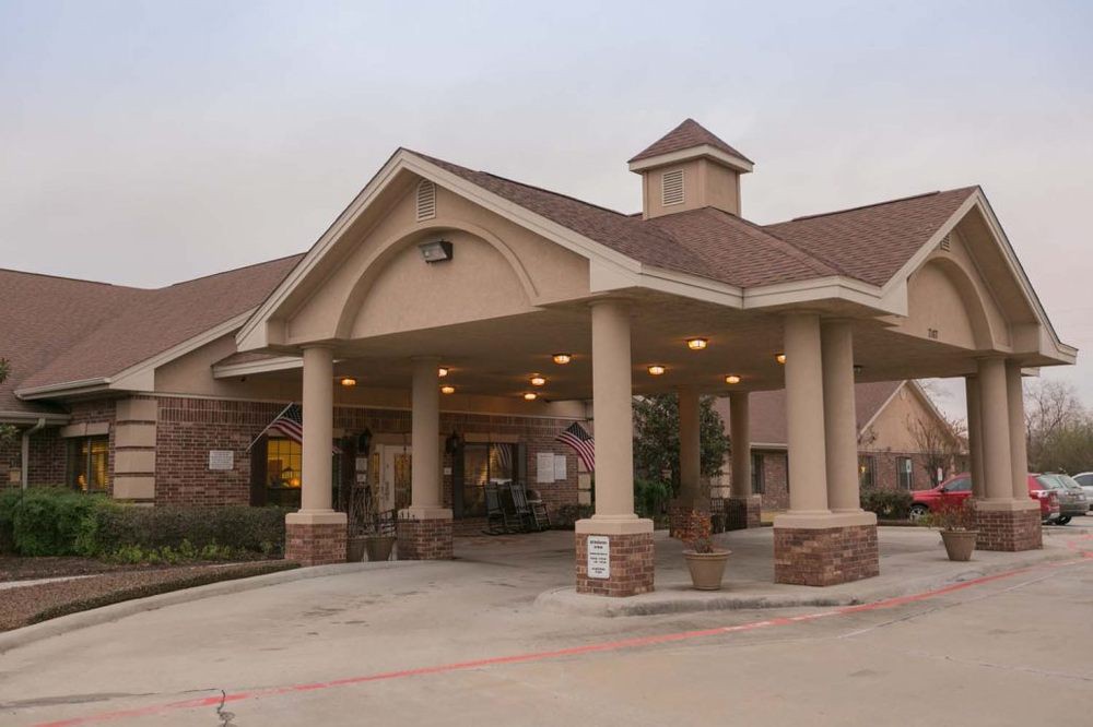 A building with a covered entrance and driveway, featuring pillars and a peaked roof.