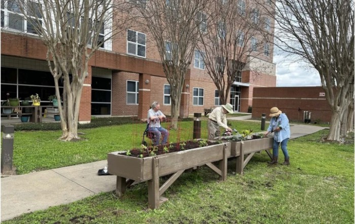 People working in a community garden with raised beds outside a building.