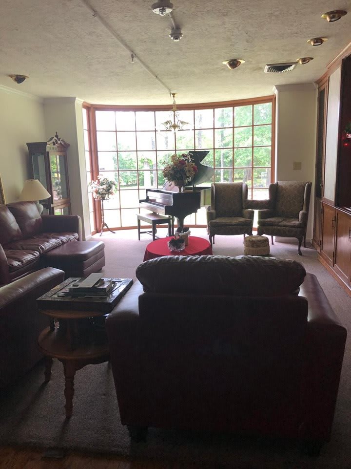 A cozy living room with a grand piano by a large window, surrounded by comfortable seating and tasteful decor.