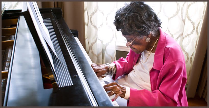 An elderly woman playing the piano with focus and passion indoors.
