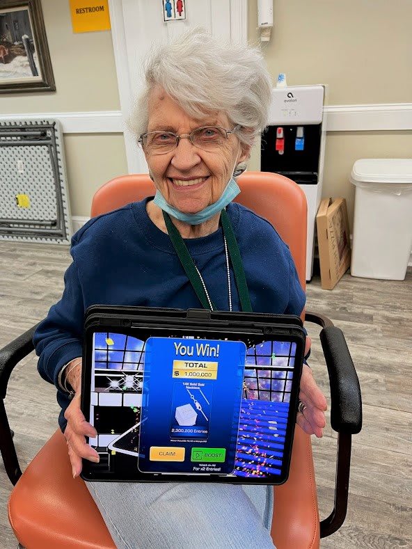 An elderly woman smiling while playing a game on a tablet indoors.