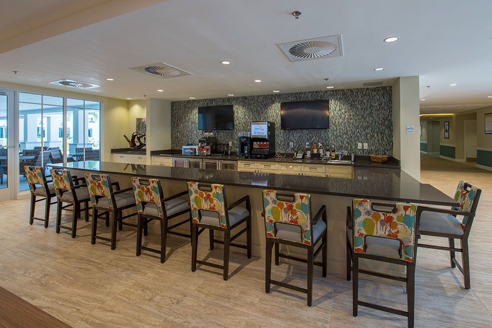 A modern bar interior with a long counter and colorful chairs.