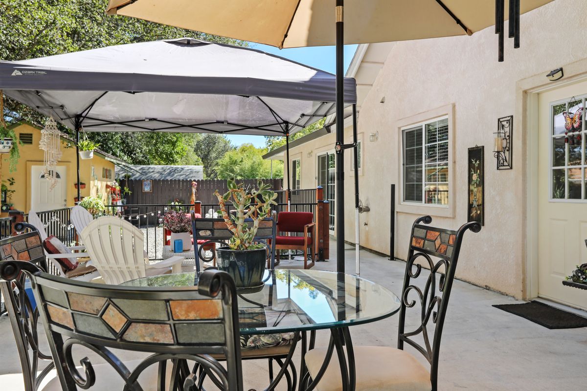 A sunny backyard patio with a glass table, chairs, and umbrellas providing shade.