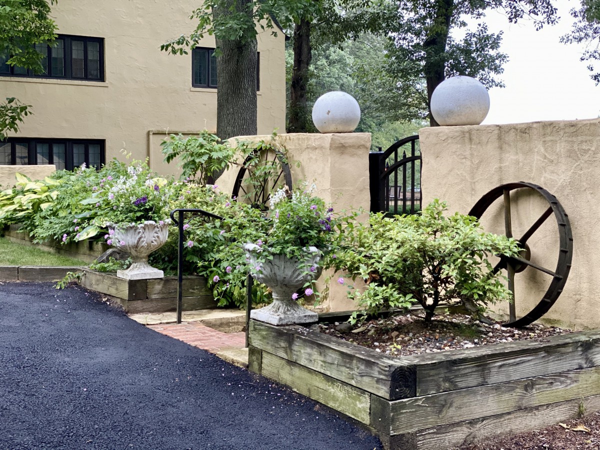 A charming garden with lush greenery, decorative urns, and architectural elements along a paved pathway.
