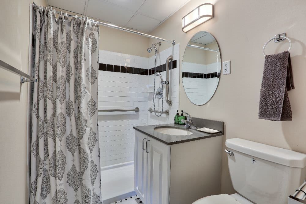 A modern bathroom with a shower curtain, sink, circular mirror, and toilet.