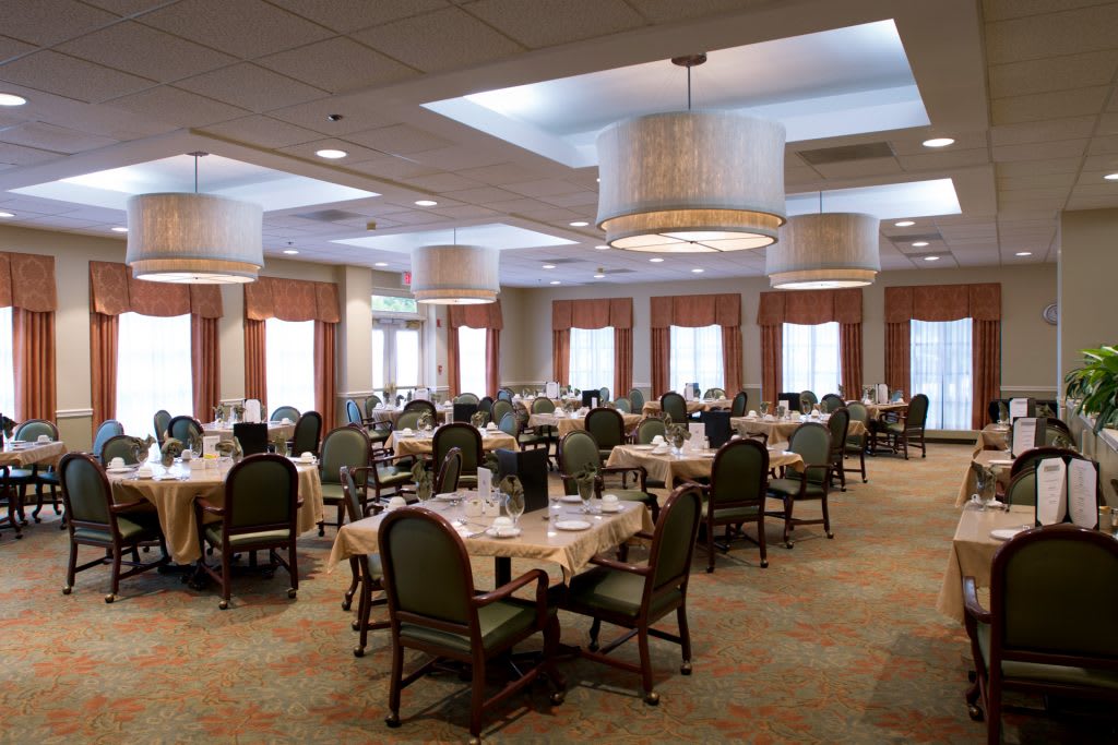 An elegantly set dining room with multiple tables and chairs, featuring soft lighting and a welcoming atmosphere.