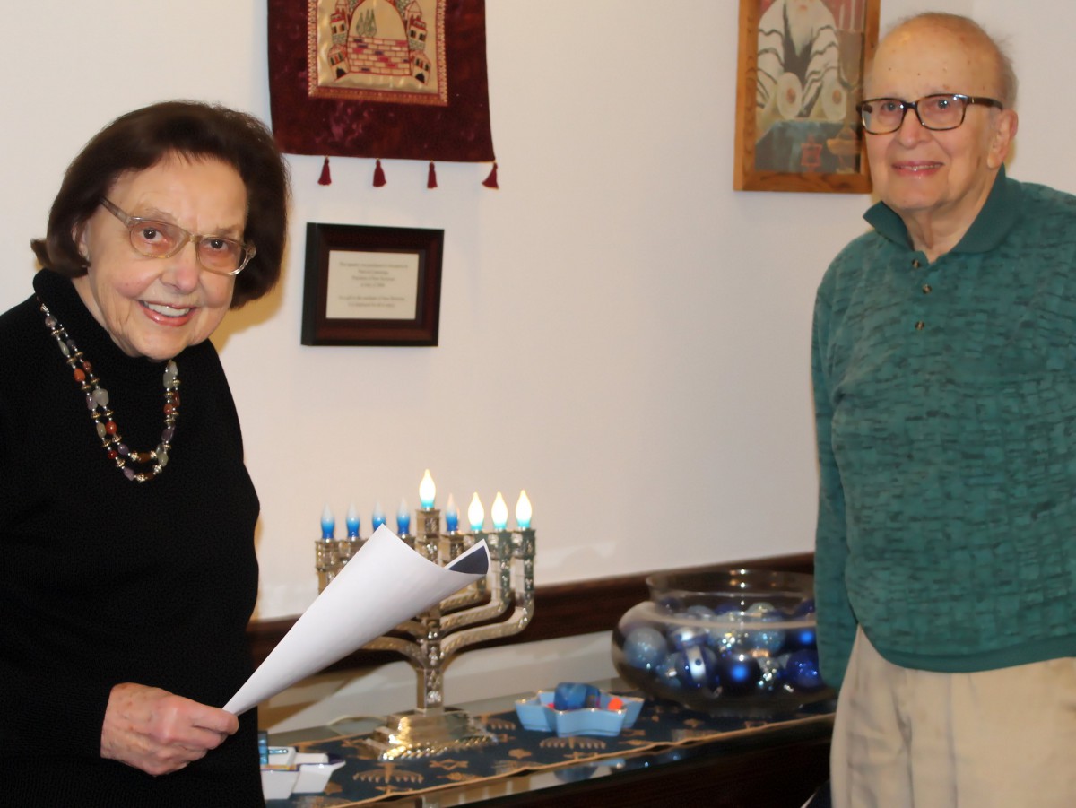 Two people celebrating Hanukkah with a menorah lit on a table.