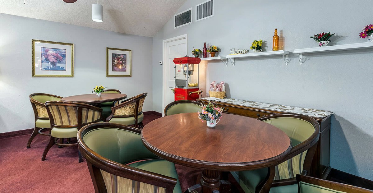 A cozy room with a round table surrounded by chairs, featuring a popcorn machine on the countertop and decorative items on shelves.