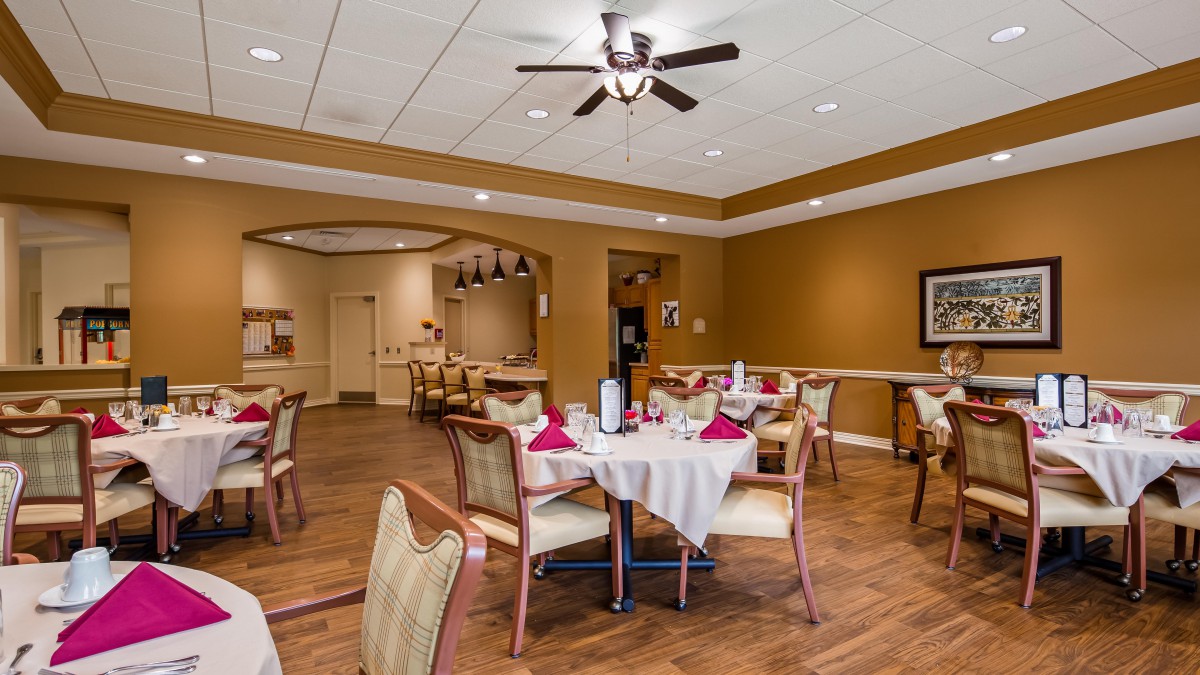 A cozy dining area with neatly arranged tables and chairs, featuring warm lighting and a ceiling fan.
