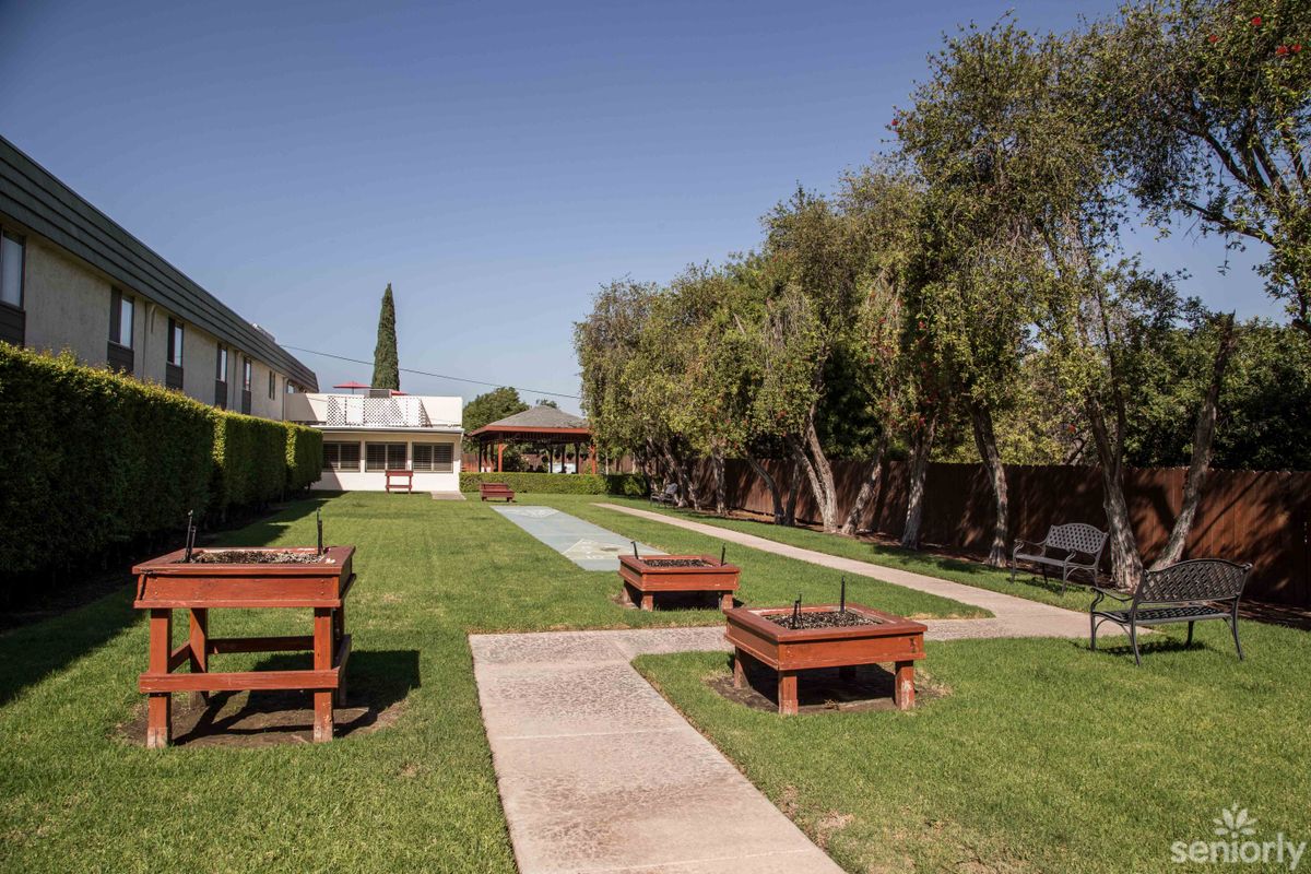 A peaceful courtyard with a grassy area, surrounded by trees and buildings, featuring benches and a paved pathway.
