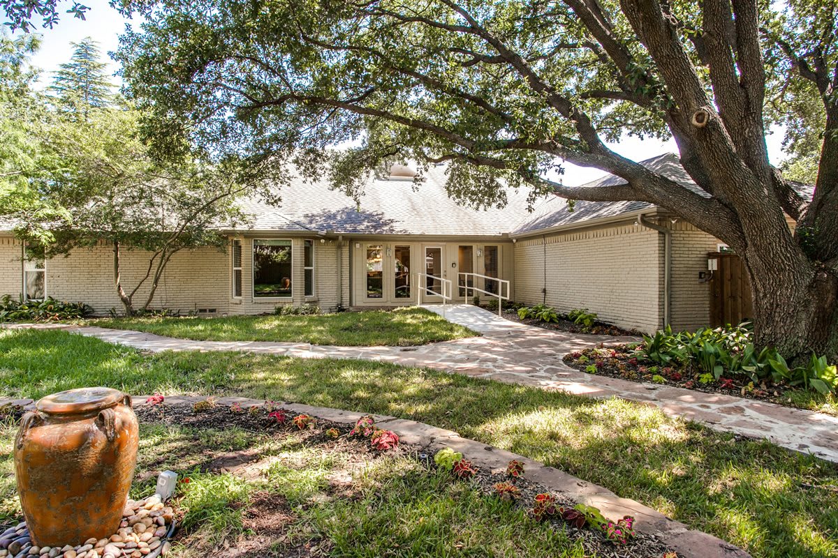 A single-story house with a large tree in the front yard and a winding pathway leading to the entrance.