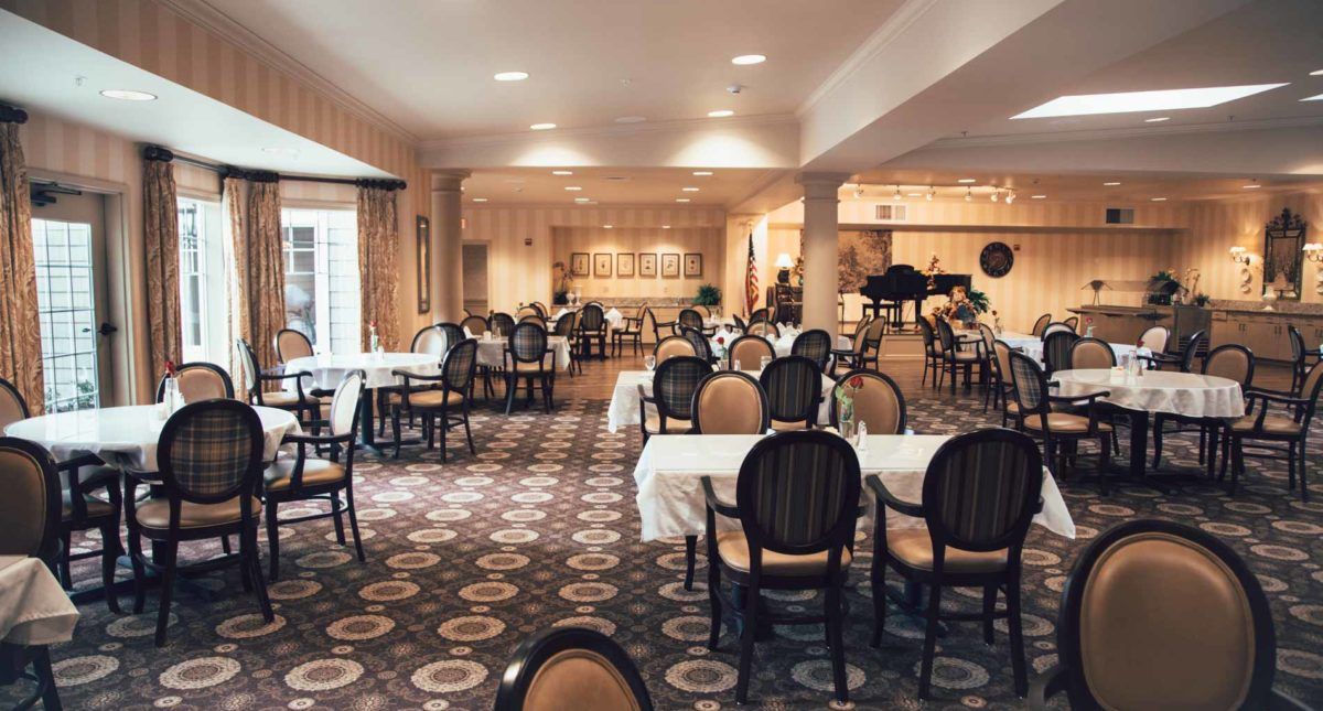 A spacious and elegant restaurant dining area with neatly arranged tables and chairs, featuring a grand piano in the background.
