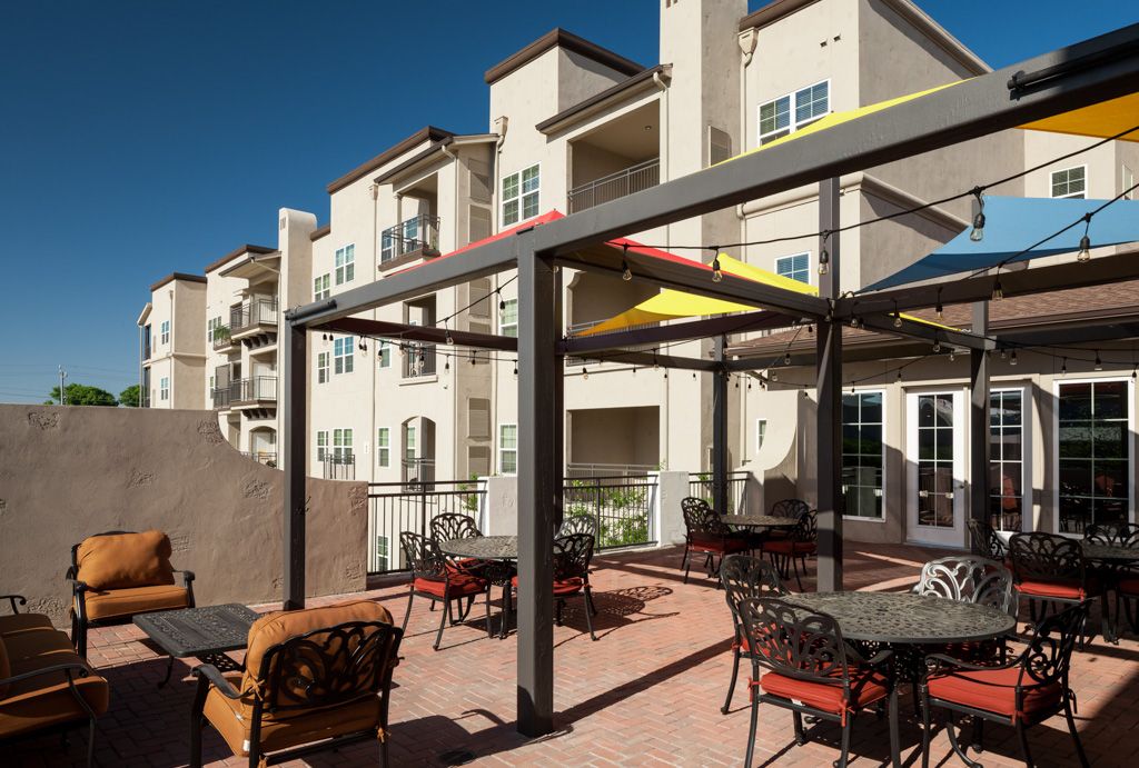 Modern apartment complex with a stylish outdoor patio area featuring seating and a pergola.